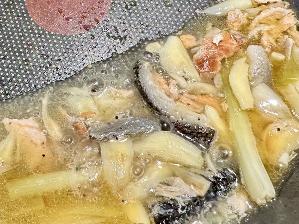 ●加5大匙煮麵熱水到炒鍋中，連同鍋中的魚皮跟鮭魚碎肉蒜瓣一起小火燉煮成淋麵高湯，帶有所有食材香氣的高湯最後要淋在冷麵上。
※鮭魚塊有撒鹽，煮麵水也有加鹽，這裡我沒再加鹽，可視個人口味斟酌添加。