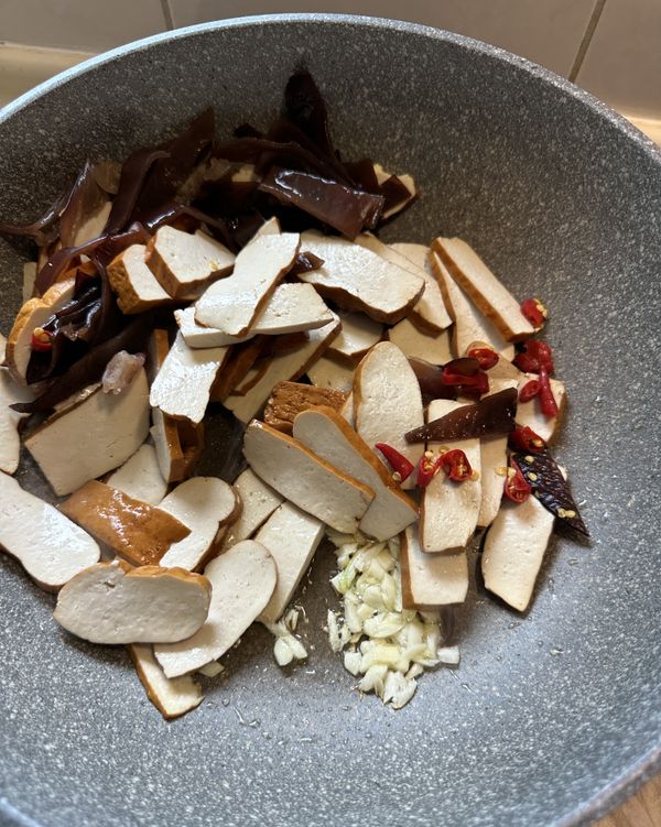 不沾鍋裡放一大匙的油開中小火，不需等油溫變高就可以將蒜末、豆乾、黑木耳、辣椒放進鍋裡加熱1分鐘，不要翻動直到聞到蒜香味⋯