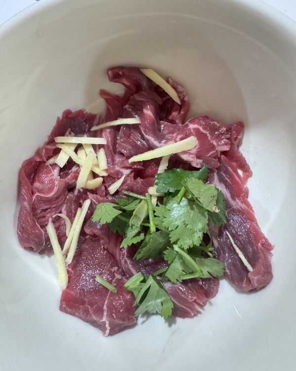 牛肉片舖在碗底，加入泡好的薑絲和香菜沫