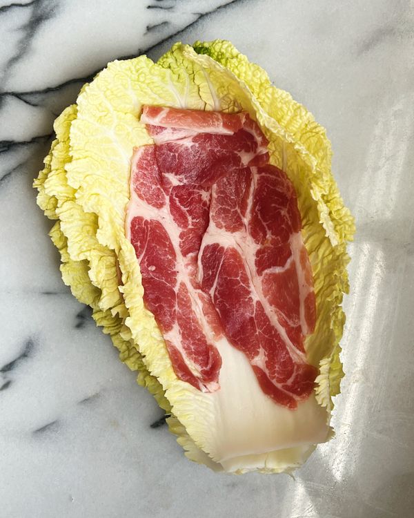 取白菜一片葉子鋪上數片豬梅花火鍋肉片。