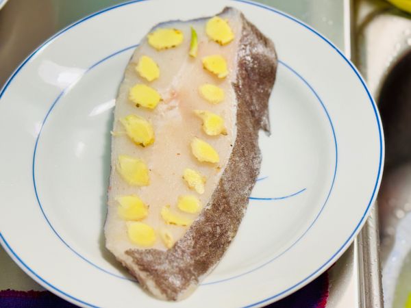 將嫩薑切片，平鋪在鱈魚片上。
