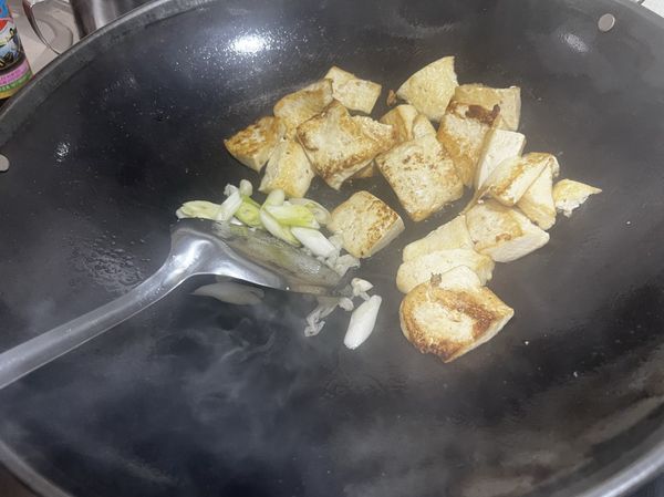 豆腐煎香後推到一旁，在另一旁爆香斜切成段的蔥白和蒜末
