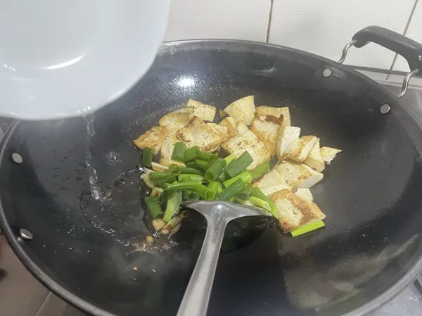 然後加入切成段的蔥綠，並且加入些許水，將所有醬料拌勻，試試鹹味，如不夠鹹的話再添鹽，並將豆腐浸入醬汁中