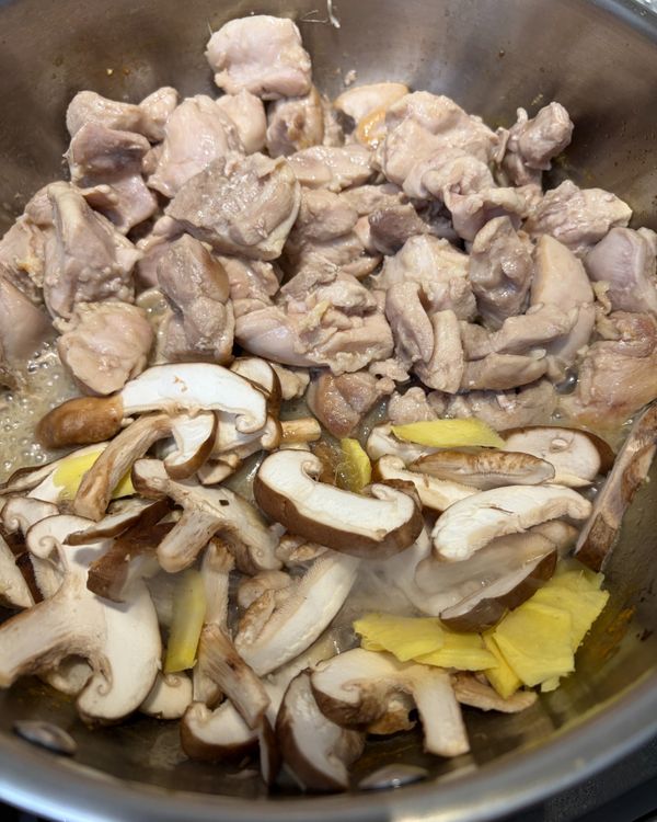 爆香薑片與香菇: 
將雞肉撥到鍋子一側，利用雞油那一側直接下薑片與香菇，中火煸炒至薑片邊緣微捲、香菇出水收縮、香氣散出，約 1–2 分鐘。全程用雞油爆香，不需額外加油。