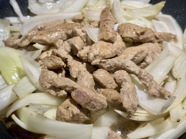 聞到蔥香再把洋蔥絲放進進來拌炒，讓洋蔥絲均勻沾滿鍋中的油脂跟肉汁，蓋上鍋蓋蒸炒2分鐘。