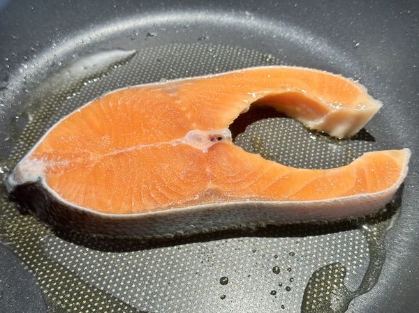 冷凍鮭魚拆封後沖洗過用廚房紙巾拭乾，兩面灑上鹽花，這樣能去腥也容易金黃上色，鍋小火加油擺進鮭魚，按下計時器。