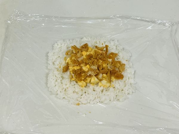 鋪好保鮮膜，鋪上一層糯米飯，在飯中央加入拌好的內餡與老油條碎