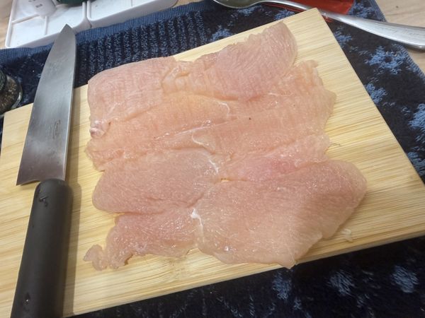 雞胸肉洗淨擦乾，從側面橫切進去（小心不要切斷，更不要像我一樣買錯買到切好的..），然後像打開一本書一樣把雞肉攤開。接著隔著保鮮膜，用肉鎚或平底鍋底輕輕把雞肉拍打均勻，讓整片肉的厚度差不多，並在雞肉兩面都撒上少許鹽巴和黑胡椒抓醃一下。