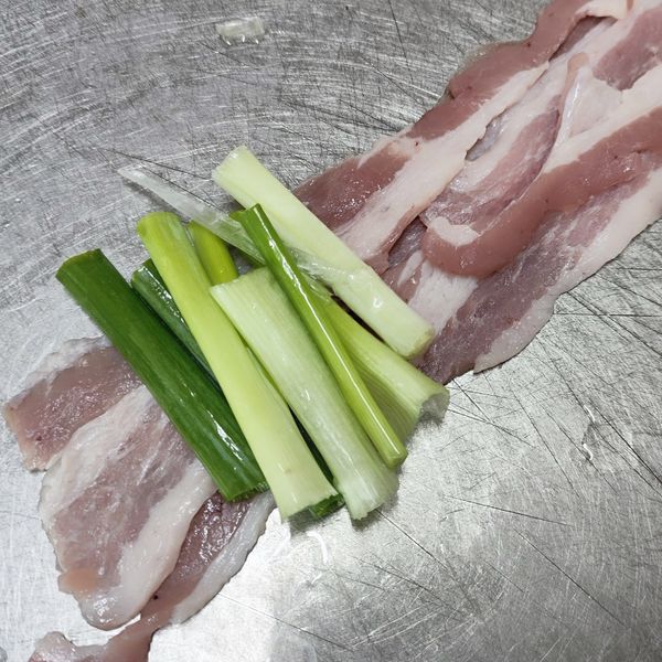 將市售的豬薄片攤開，如果肉片比較短，可以使用交疊的方式增加捲肉的長度，放上5-6跟的蔥段，記得挑選有白有綠的蔥段更美味。