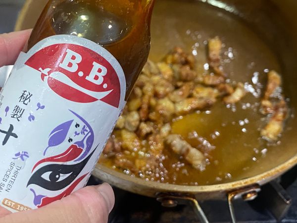 中火翻炒約十分鐘，待五花肉層現金黃色，加入秘製十三香、白胡椒，連同豬油一起包裹