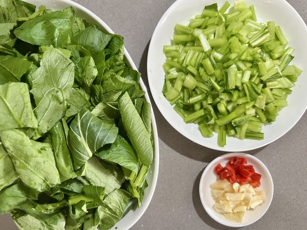 小松菜烹調前將根部切除，葉梗每一葉在流動的清水下沖洗，去除表面殘留農藥。菜洗好再切，菜葉跟菜梗熟成度不同分開擺放；蒜瓣跟小松菜一起泡洗拍碎切末。