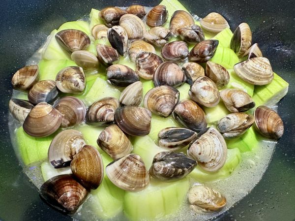 ●4分鐘絲瓜熟了會有湯汁出現，打開翻拌撒上(白胡椒粉)，加(蛤蜊)均勻分布在鍋中，蓋鍋一起煨煮。
