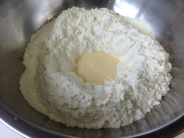中筋麵粉、低筋麵粉、泡打粉過篩後和鹽、糖混合均勻。蛋打散後和鮮奶混合成奶蛋液。如圖將麵粉堆中間挖一個洞，奶蛋液邊倒入邊將麵團混合。