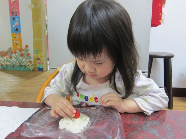拌入鷹牌煉奶的米飯，取適量鋪平在塑膠袋上，擺上1顆新鮮草莓。
