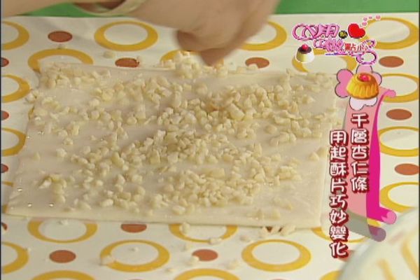 在抹上糖霜的起酥片上均勻灑上杏仁角，利用起酥片附的隔層紙覆蓋在上面輕壓一下使杏仁角能附著。