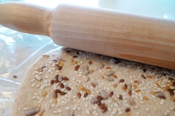 擀麵棍輕滾，將芝麻壓進麵團裡。