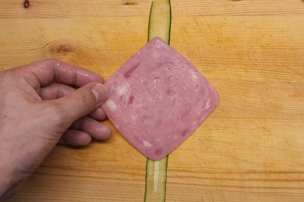 放上一條小黃瓜片在砧板上，再疊上一片火腿。