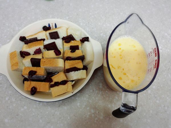 巧克力片和吐司切成適當大小 , 烤模塗上一層薄奶油 , 將吐司和巧克力交錯排放 , 接著灑上適量蔓越莓乾 ; 將布丁液材料混合拌勻並且過篩 , 接著倒入烤模中 。