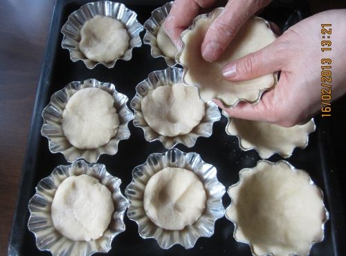 將塔皮的材料全部放在一個大碗中，用手充分抓拌成麵團，撒上一些麵粉，操作時才不會粘手。將麵團平均分成9份，雙手慢慢擠壓麵團直到塔皮充滿整個模具。務必厚薄均勻！