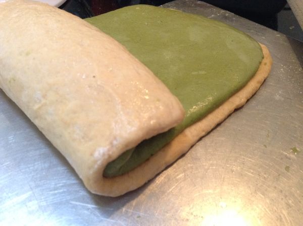 [抹茶麵團] [南瓜麵團]麵團上灑些手粉，用桿麵棍桿成長形，寬度與烤盒同寬。麵團表面噴些水，將兩麵團重疊，並輕輕捲起。