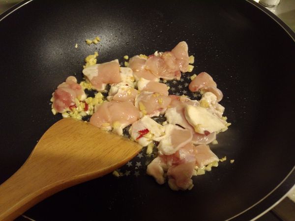 爆香大蒜及辣椒後，加入雞肉拌炒至半熟。