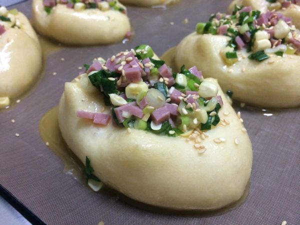 取出的麵團刷上一層蛋液，再將餡料滿滿的裝在十字剪開處，最後撒上白芝麻