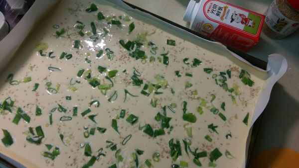 將拌勻之麵糊倒入烤盤抹平，撒上葱花.白芝麻