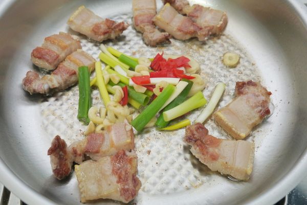 將五花肉推至鍋中一旁，再利用乾煸出來的五花肉油脂爆香蔥段、蒜片、薑片、辣椒丁。