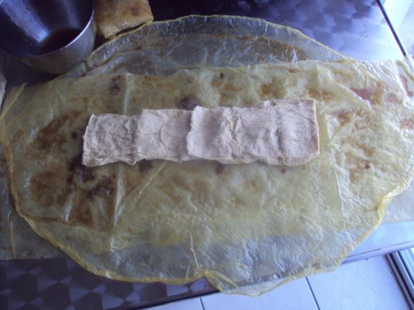 一張腐皮從中剪開,成兩個半圓形,在面上抹些綜合調料,使腐皮略微濕潤,再疊上另一片腐皮,也是抹些綜合調料,兩片豆包攤開放中間.