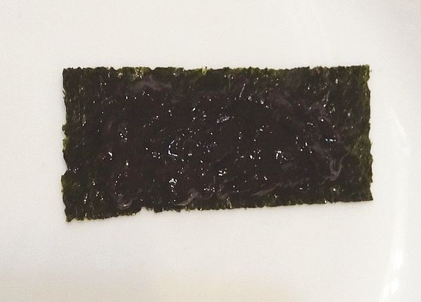 取一片海苔，將預先煮好放涼的紫米飯適量平舖在海苔上。