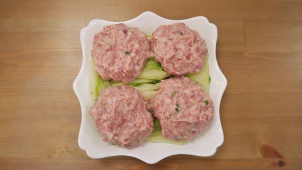 步驟3：
取蒸盤鋪上芽白心擺上肉丸入蒸鍋蒸25分，另用高湯汆燙洗淨的青江菜備用。