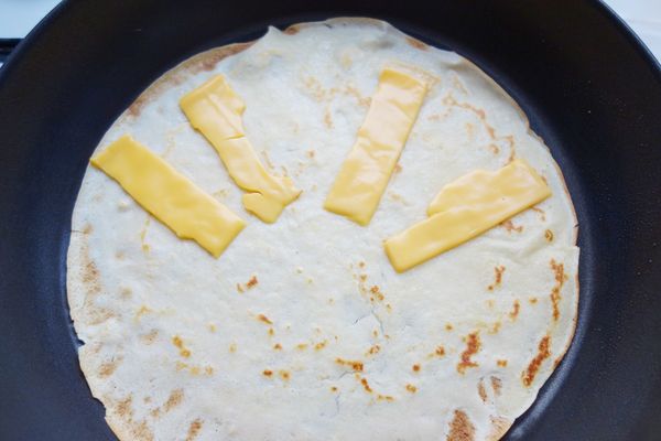 關最小火，將餅皮再翻面(內面朝上)，擺上起士片煎至起士融化把餅皮小心移至盤/板上。重覆做法6和7做下一張餅皮