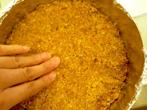 將餅乾屑倒入圓形烤模中，均勻鋪滿，再以手緊緊壓平密實，鋪上保鮮膜放置冰箱冷藏約15分以上使其硬實
