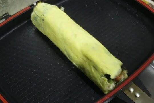 打勻一顆蛋，放入平底鍋中，蛋呈現半熟時，把飯捲放下去，拿起木匙，一隻手壓，一隻手邊翻，讓蛋附著在飯捲上，再讓它在熱一下，切開來，就完成了