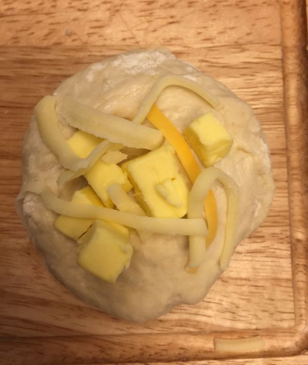 用手輕輕將麵糰拉開包入奶油丁、起司絲，再整成圓形，收口朝下