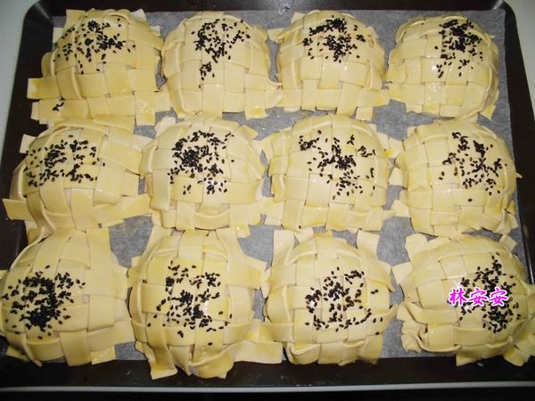 在起酥片上方，再刷上全蛋蛋液，安安刷了兩次。
第一次刷完12個麵包，再回頭刷第二層。
最後再灑上黑芝麻。