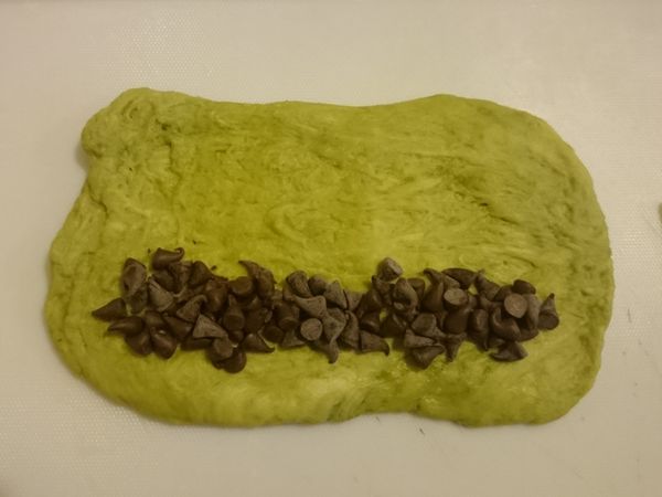 將麵糰擀成長方型，在一邊鋪上朱古力粒，然後捲起封好。