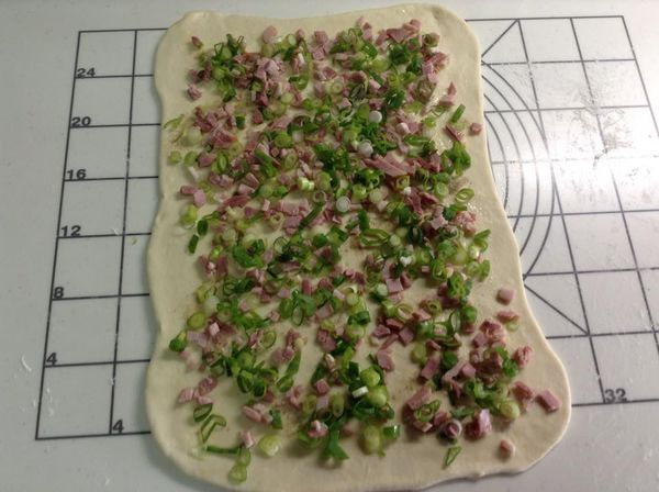 餅皮上面塗上薄薄一層麻油，撒上胡椒塩、火腿丁、葱丁、白芝蔴，然後開始捲成棒狀。