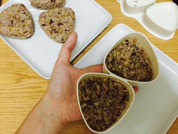 可準備一小碗鹽水，手稍沾鹽水後，將拌過香鬆的五穀米裝入飯糰塑型的容器裡。