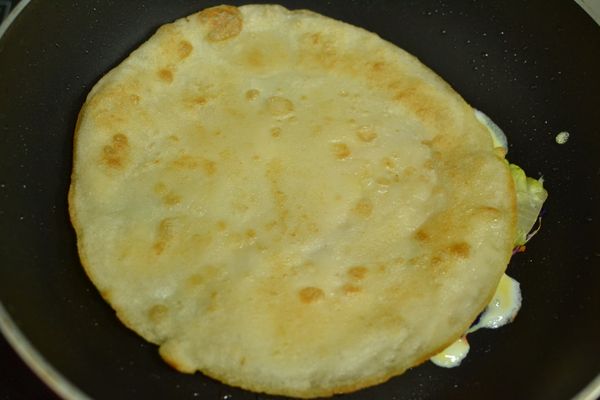 底部稍微凝固後將煎好的餅皮鋪上，用鍋剷稍微壓一下，翻面淋上醬油與辣椒醬。