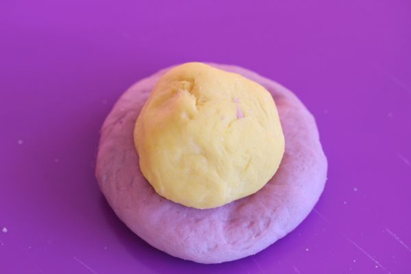 將發酵好的紫薯麵糰分成一份65g大小滾圓，南瓜麵糰分成一份45g大小滾圓，將紫薯麵糰壓扁後中心放入南瓜麵糰