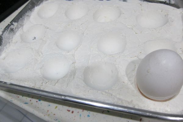 把超熟的玉米粉鋪在鐵盤上，拿一顆乾淨的雞蛋，在玉米粉上壓出半圓形