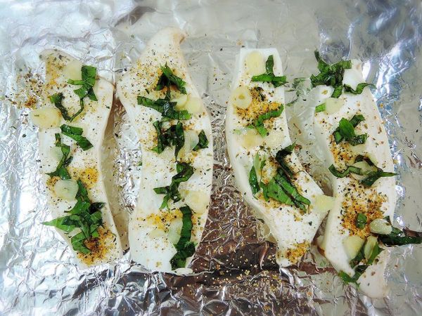 把對半切的杏鮑菇擺上烤盤，撒上橄欖油、雞肉鹽後擺上九層塔及大蒜