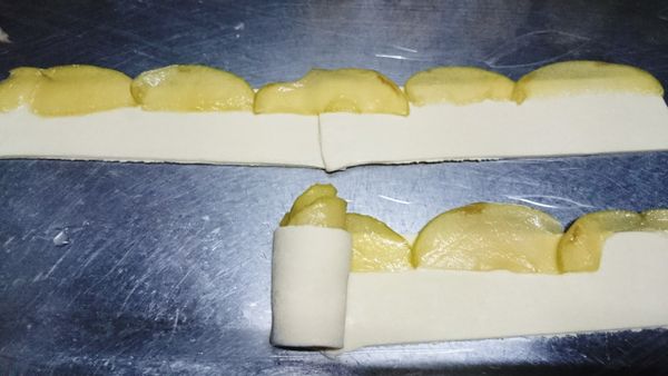 冷凍起酥片退冰後,切三等份成為三長條狀,二長條接在一起,讓長度變長;軟化的蘋果鋪在起酥皮上方,蘋果皮約露出起酥皮1/3,鋪排好後捲起