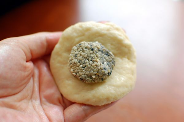 開始製作小豬囉！首先取出一小坨麵糰，稍微壓平成手掌大小，然後將芝麻內餡放置中央，包覆起來