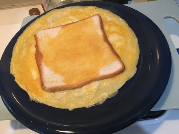 蛋皮煎至可以自由在平底鍋滑動時，拿一個大盤子將蛋皮滑至盤上，吐司那面要朝上。