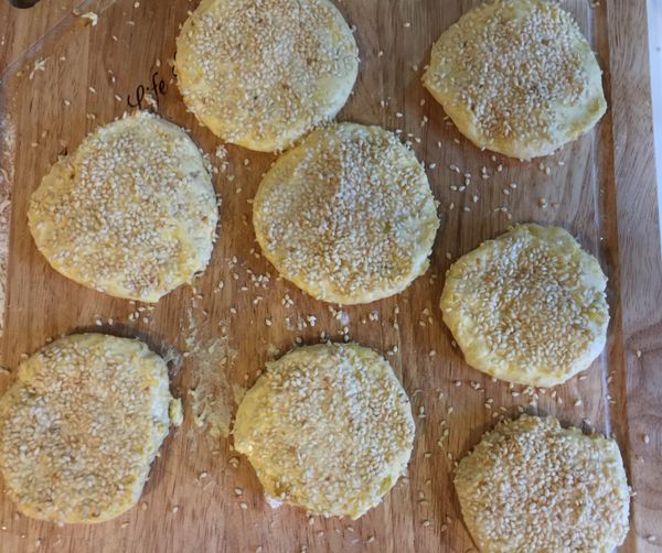 加入糖粉與麵糰揉勻，均分成八小塊，搓圓壓扁，在其中一面抹上少許水，加上芝麻