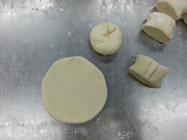 完成上述的部驟後麵團的時間也差不多到了。在桌上均勻灑上低筋麵粉(另外的份量)，放上麵團先搓成長條狀再切割成如圖的塊狀，然後用桿麵棍（或圓條形器具皆可）桿成如圖中像放大版的水餃皮