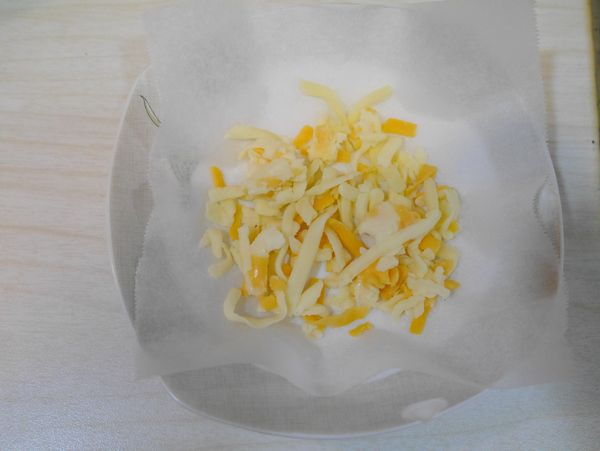 取一盤子，鋪上一張烘焙紙，放上少許起司絲，要能放上蘇打餅的大小，起司絲要鋪平不要重疊，這樣餅才會薄脆