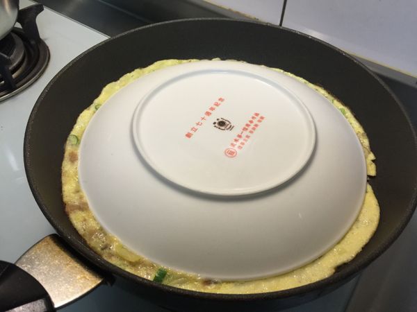 拿一個大盤子，將盤子倒蓋在蛋皮上後，迅速的把蛋皮倒扣在盤上，然後以45度角的方向，把蛋皮輕滑入平底鍋內，一樣用文火將另一面煎至金黃